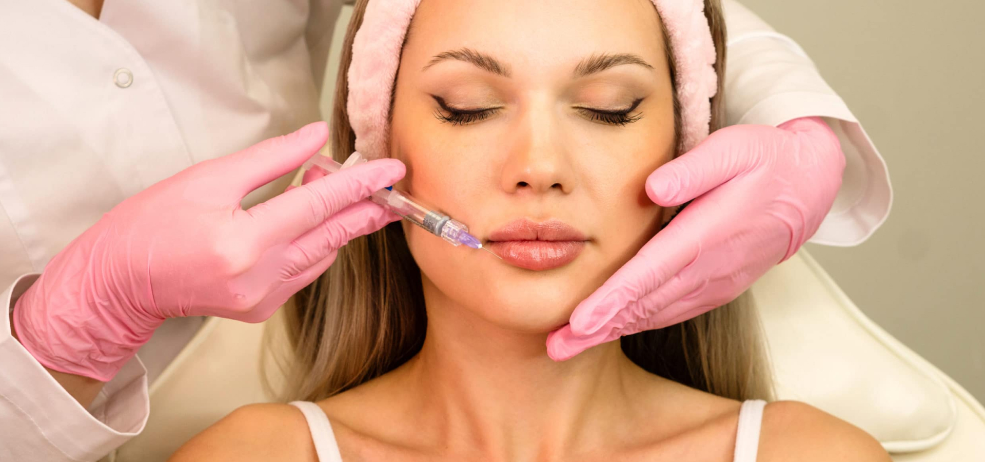 Woman receiving a lip injection from a professional wearing pink gloves.